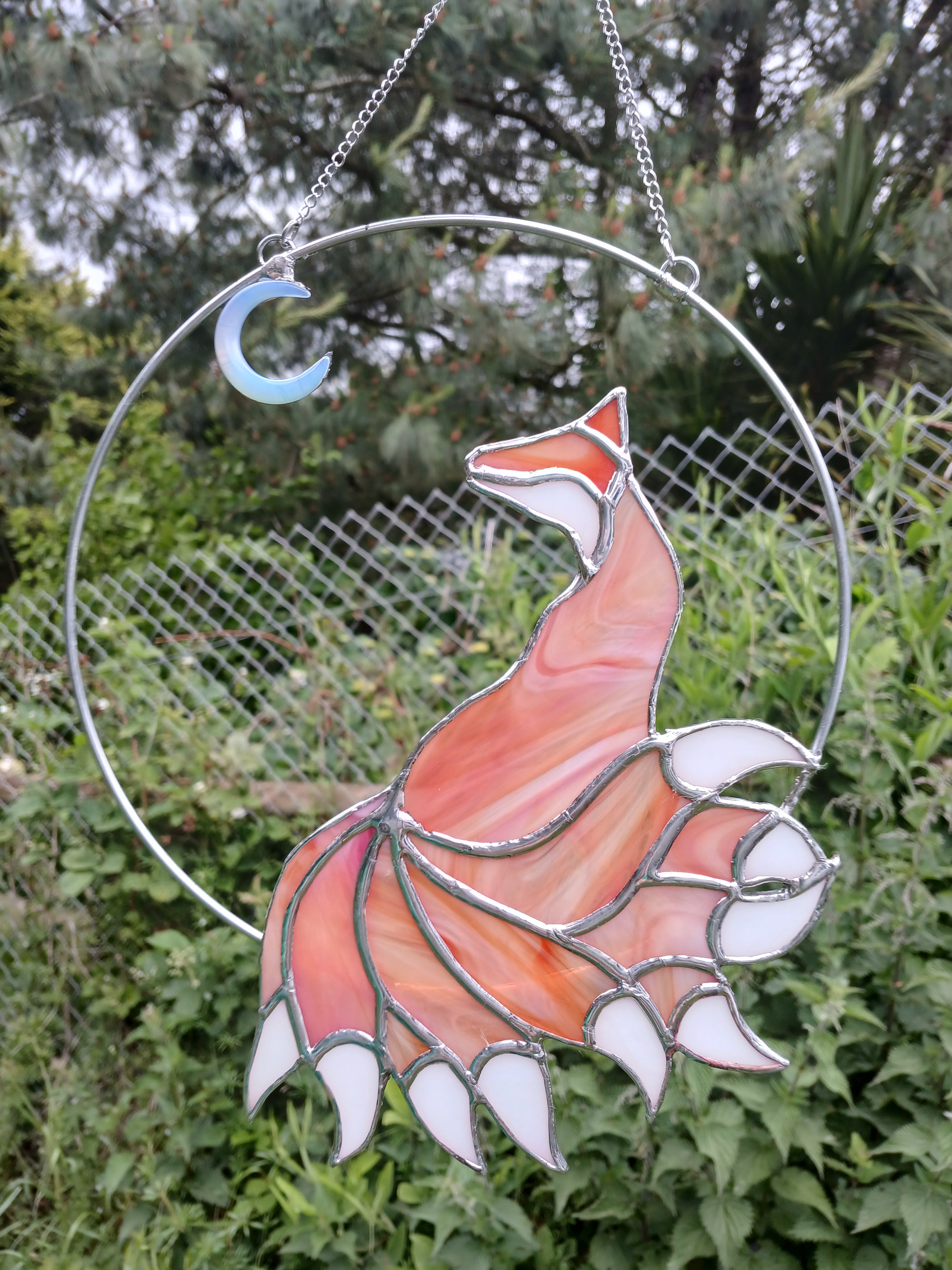 Stained glass fox suncatcher hanging against a green foliage background